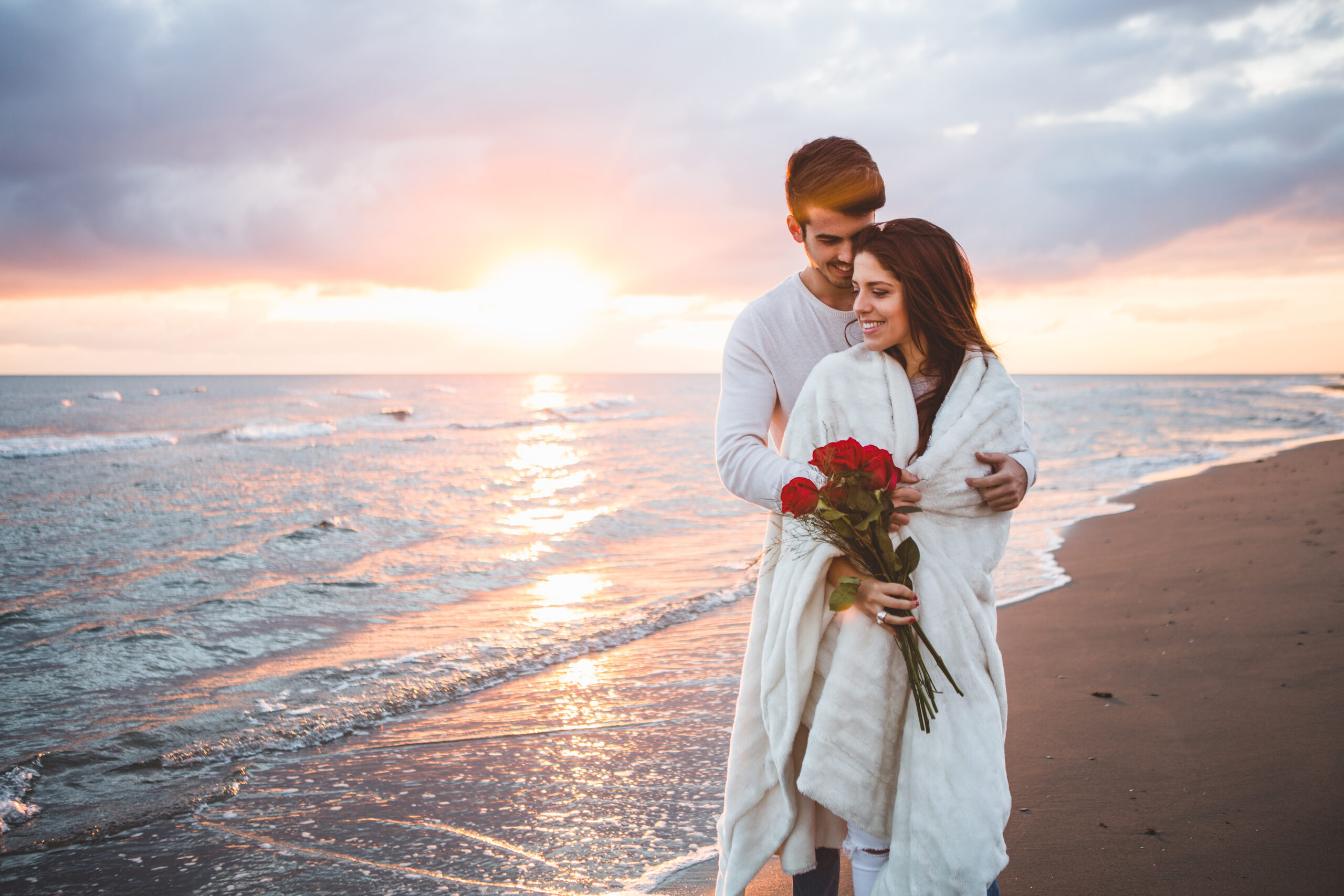 couple-walking-beach-with-bouquet-roses-sunset